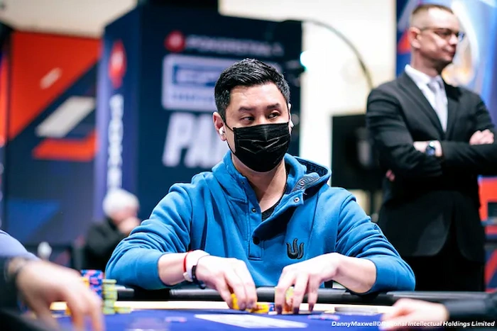 Punnat Punsri, Thai high-stakes poker pro, masked and focused at the EPT Paris table in a blue hoodie, handling chips with stacked towers in front, branded PokerStars backdrop behind him. 