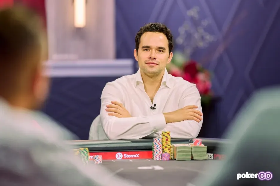 Alan Keating sitting at a high-stakes poker table with arms crossed and chip stacks in front of him