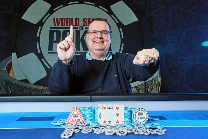 Frank Koopmann holding up his WSOP Europe 2026 bracelet with his winning A-4-4-3 hand displayed at the Hilton Prague
