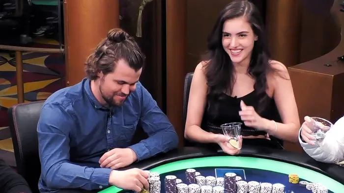 Chess world champion Magnus Carlsen and streamer Alexandra Botez laughing at a Hustler Casino Live poker table behind stacks of chips