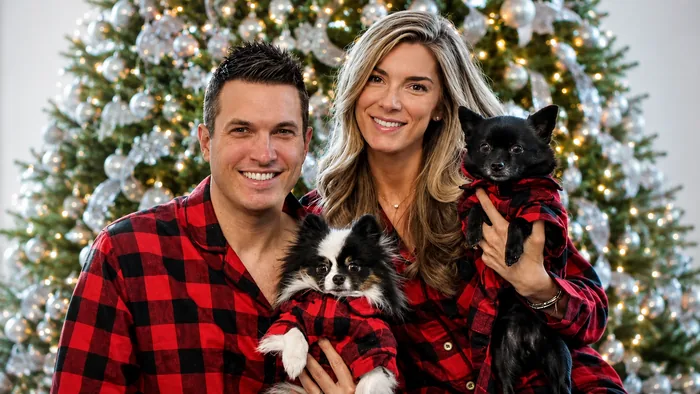 Doug Polk and Kaitlin Polk Christmas Photo Doug Polk and his wife Kaitlin Polk in matching red plaid pajamas holding two small dogs in front of a Christmas tree, the family photo Doug shares with fans