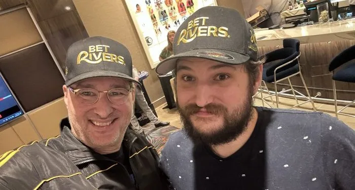 Phil Hellmuth and one of his sons smiling in matching caps in a selfie taken at a poker room